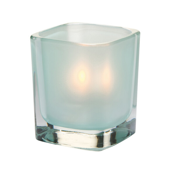 A Hollowick Tetra seafoam glass square votive candle holder with a lit candle inside.