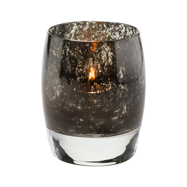 A Hollowick Contour antique black glass votive with a lit candle inside.