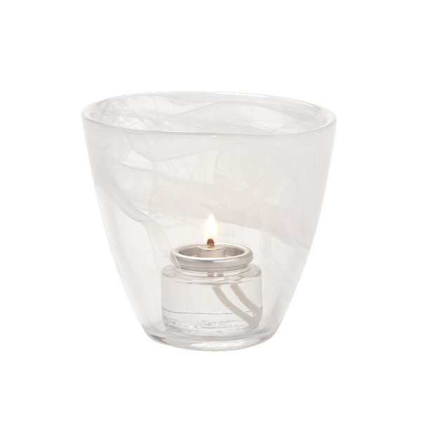 A lit white candle in a Hollowick glass votive holder.
