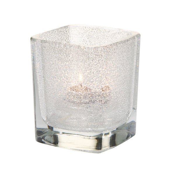A Hollowick Tetra clear glass square votive candle holder with a lit candle inside.