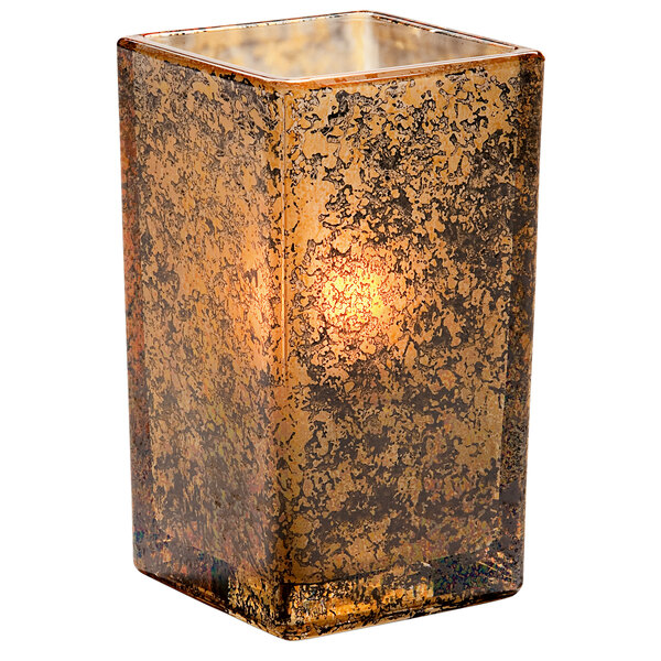 An Antique Gold square glass votive holder with a lit candle inside.