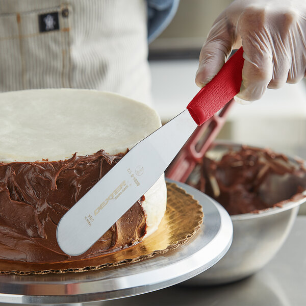 A person using a Dexter-Russell baking spatula with a red handle to frost a cake.