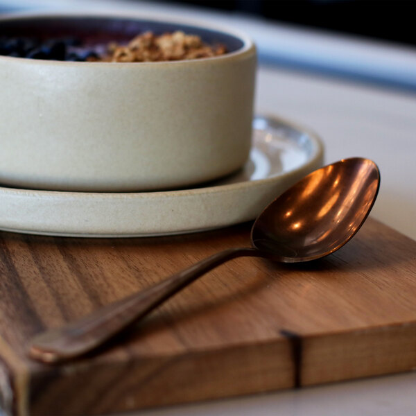 A bowl of cereal with blueberries and a Sola vintage copper coffee spoon on a wooden table.