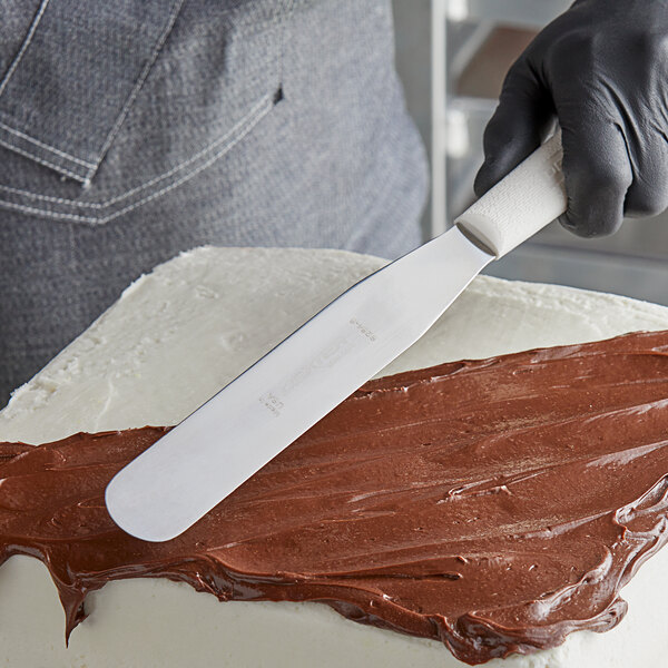 A person using a Dexter-Russell Sani-Safe straight icing spatula with a white handle to spread chocolate frosting on a cake.