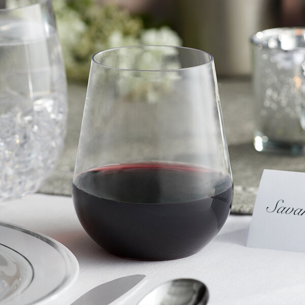 A Visions heavy weight clear plastic stemless wine glass filled with red wine on a table.