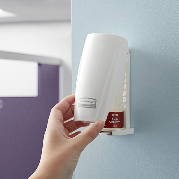 A hand holding a white plastic container on a wall.