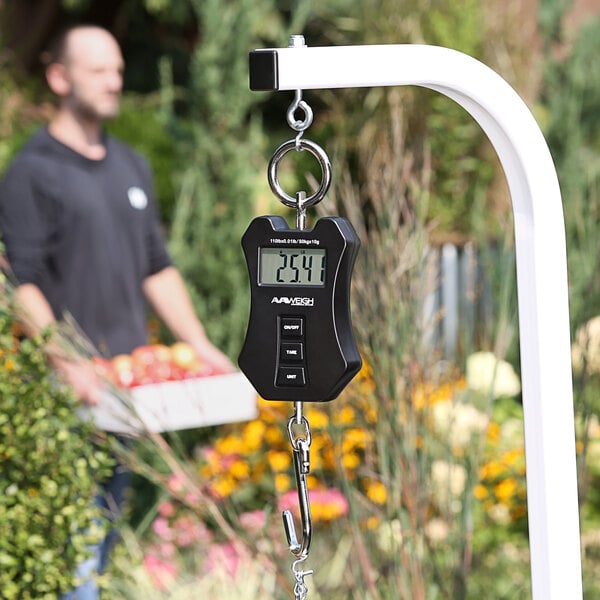 A man holding a black AvaWeigh digital hanging scale.