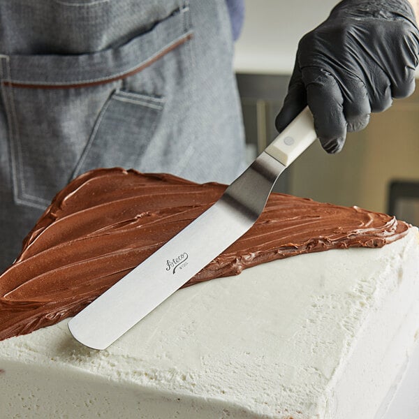 An Ateco offset spatula with chocolate frosting on a cake.