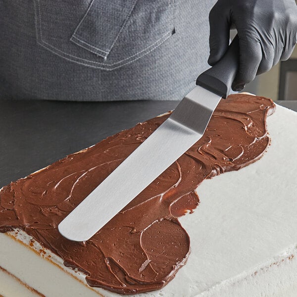 A person using a Fat Daddio's offset spatula to cut a chocolate frosted cake.