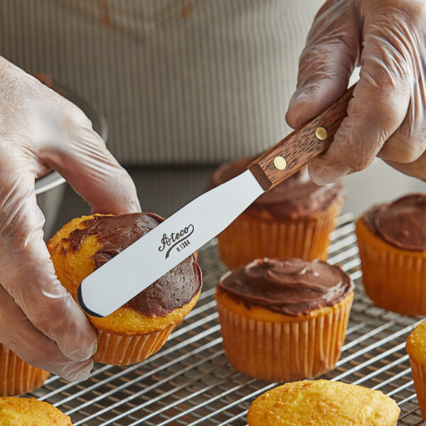A person using an Ateco straight baking spatula to frost a cupcake.