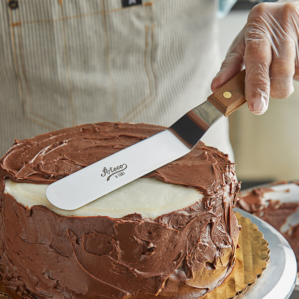 An Ateco offset baking spatula with a wood handle being used to cut a cake.