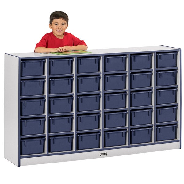 A young boy in a red shirt standing next to a Rainbow Accents navy storage cabinet with trays.