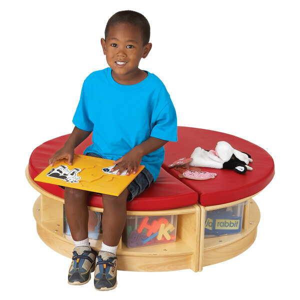 A child sitting on a round red cushion at a Jonti-Craft Read-a-Round table with a puzzle.