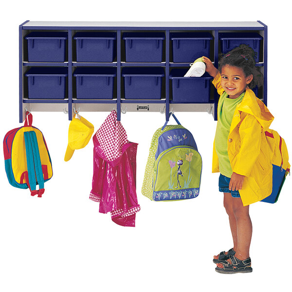 A little girl in a yellow raincoat putting a spray bottle in a blue cubby.