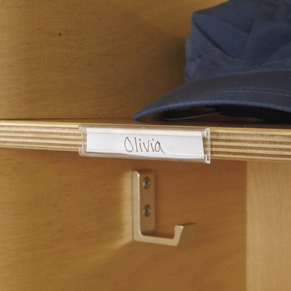 A clear plastic name tag holder on a wooden shelf holding a name tag.