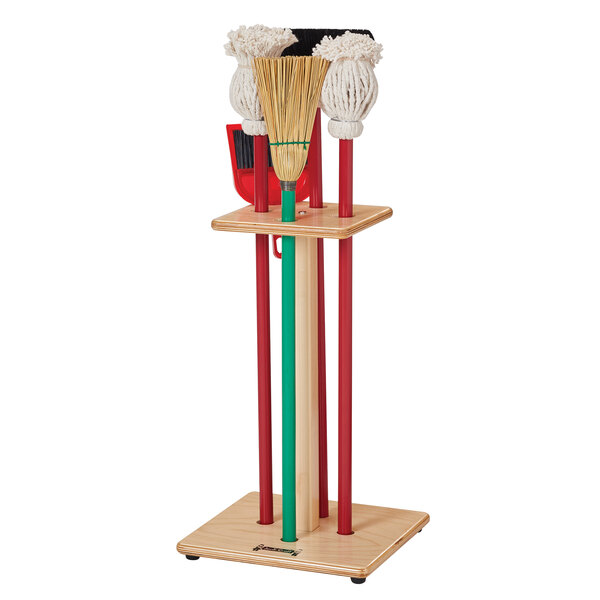 A Jonti-Craft wood rack holding six children's housecleaning pieces, including three brooms and three mops.