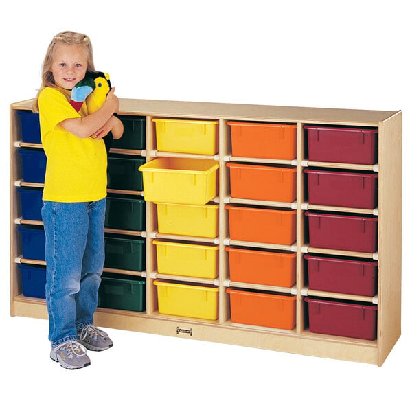 A young girl holding a stuffed animal standing next to a Jonti-Craft mobile wood storage unit with orange cubbies and black trim.