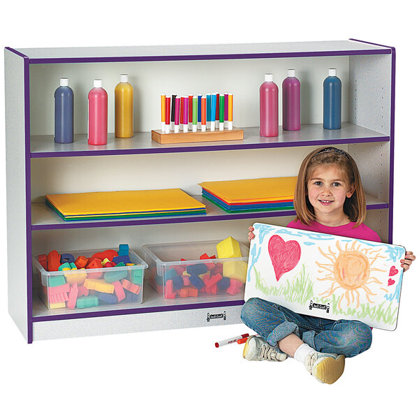 A young girl sitting on the floor holding a picture in front of a purple and gray Rainbow Accents bookcase.