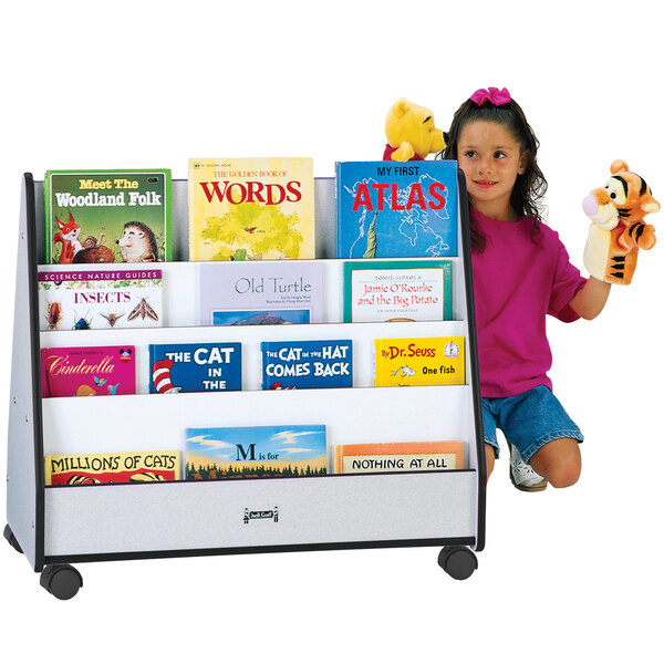 A girl sitting next to Rainbow Accents double-sided book rack with books on it holding a tiger puppet.