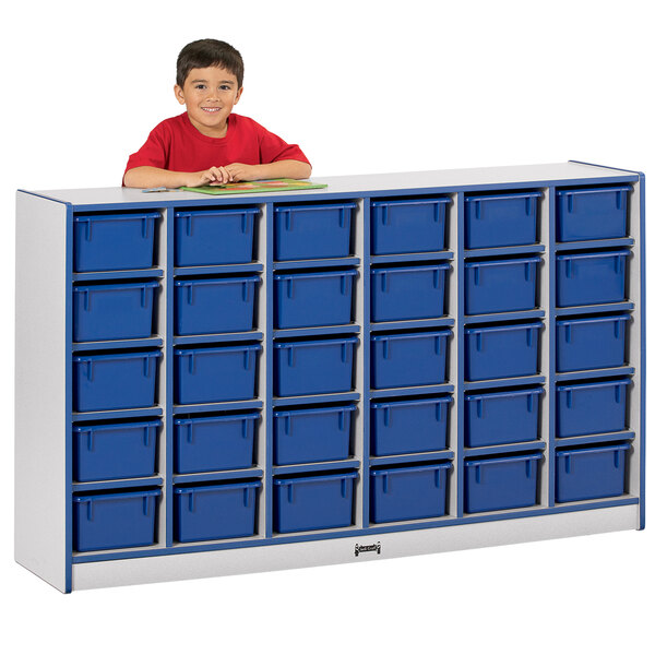 A young boy in a red shirt standing next to a blue Rainbow Accents storage cabinet with cubbies.