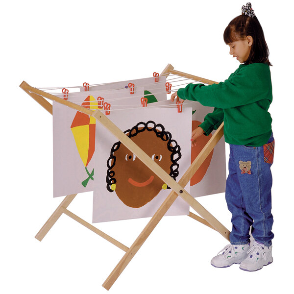 A little girl using a Jonti-Craft wood paint drying rack to dry a picture.