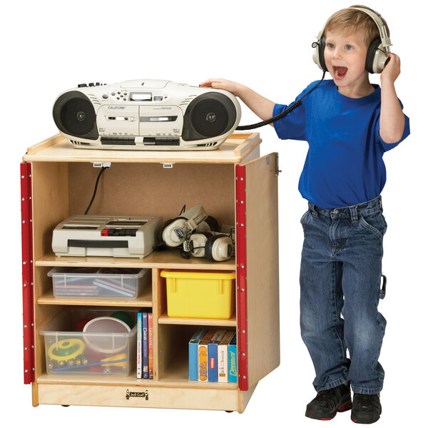A boy using a Jonti-Craft wood media cart while wearing headphones and holding a radio.
