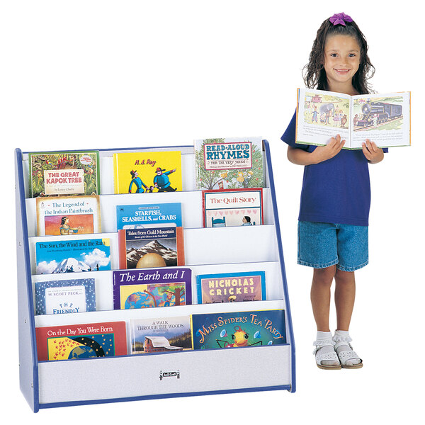 A young girl standing next to a blue Rainbow Accents book rack holding a book.