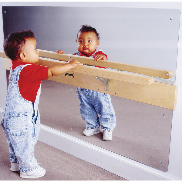 A baby standing in front of a Jonti-Craft Infant Coordination Mirror with pull-up rail.