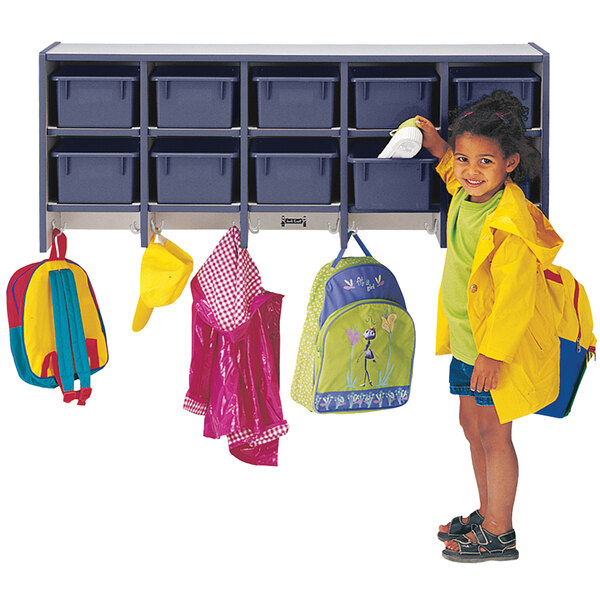 A little girl standing next to a Rainbow Accents navy blue wall-mount coat rack with a yellow jacket hanging from it.