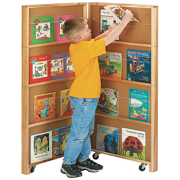 A boy standing next to a Jonti-Craft mobile library bookcase filled with books.