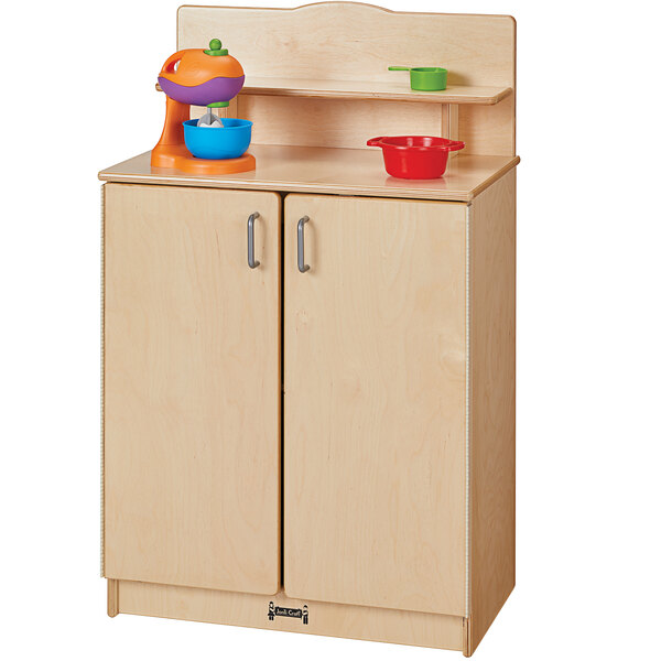 A Jonti-Craft wooden school age kitchen cupboard with a mixer and bowls on it.