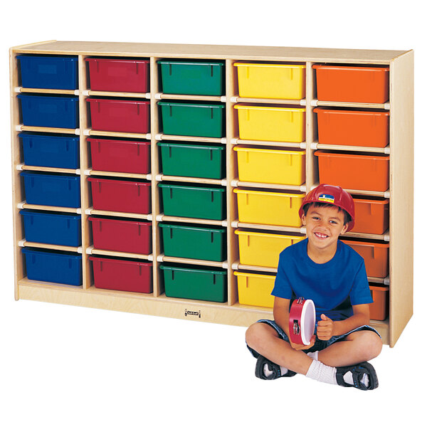 A boy sitting on the floor in front of a Jonti-Craft wood storage unit with orange, yellow, and red bins.