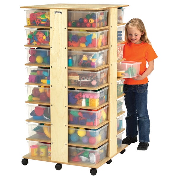 A girl standing next to a Jonti-Craft wood tub storage tower with clear plastic containers inside.