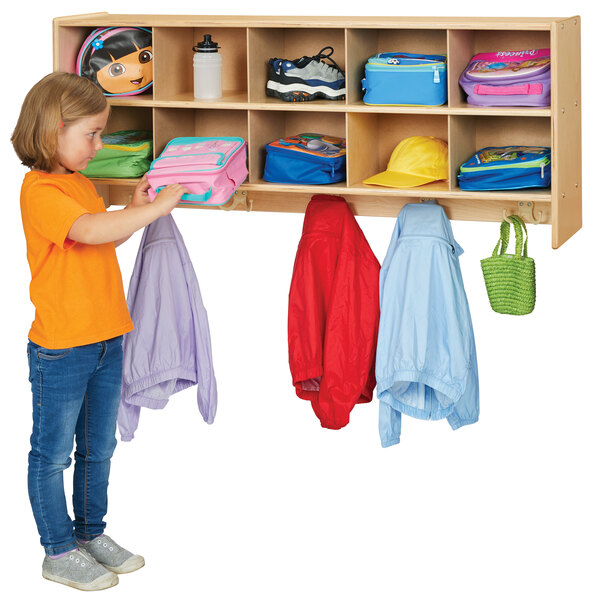 A child in a yellow shirt putting purple and pink clothes in a green bag hanging on a Young Time natural wood coat locker.