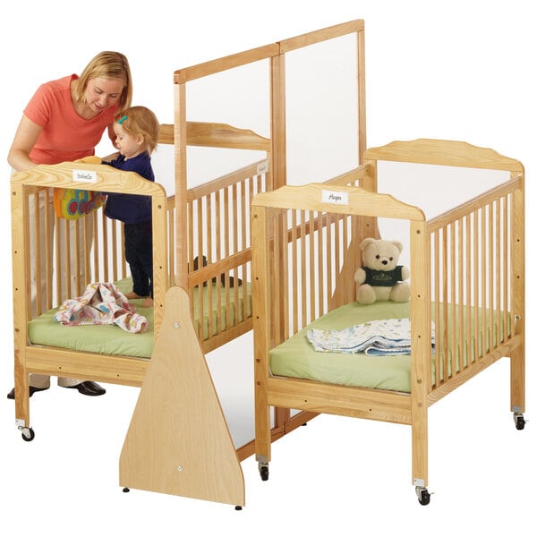 A woman standing next to a baby in a Jonti-Craft large crib divider.