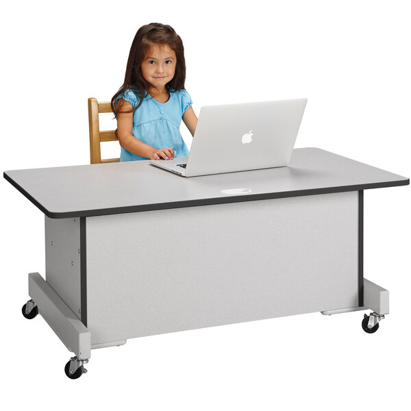 A young girl sitting at a Rainbow Accents computer desk using a laptop.