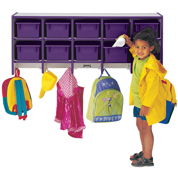 A little girl wearing a yellow rain coat putting a spray bottle into a purple and gray Rainbow Accents wall-mounted cubby with double hooks.