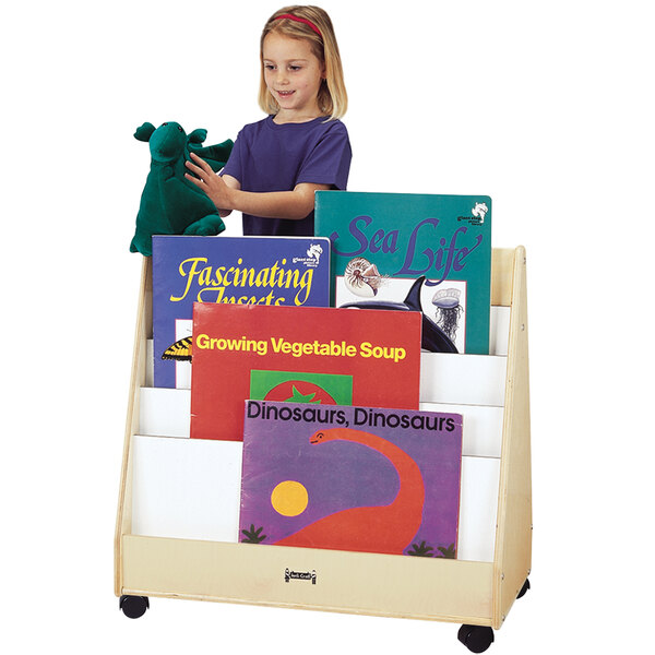 A young girl in a purple shirt holding a Jonti-Craft mobile double-sided wood book rack filled with books.