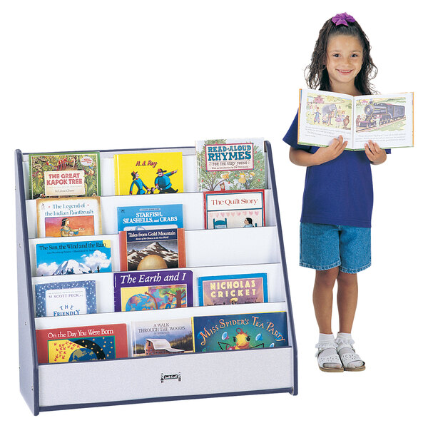 A young girl standing next to a navy blue Rainbow Accents book rack filled with books.