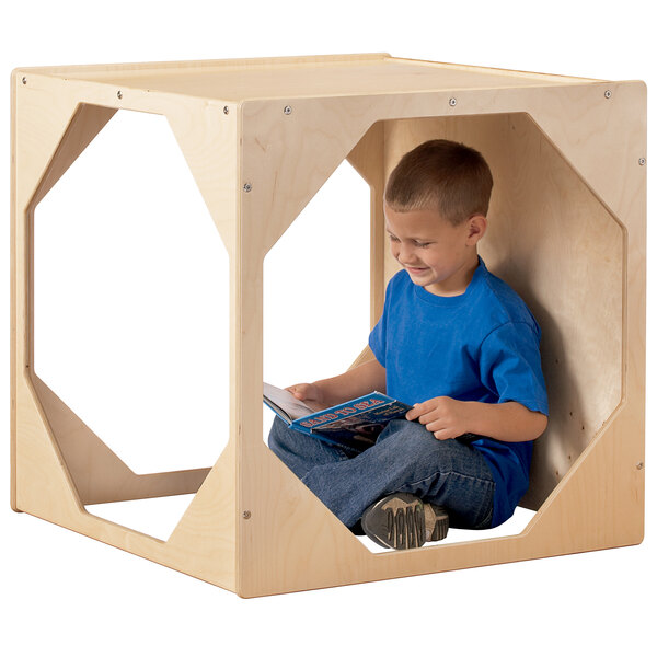 A young boy reading a book in a Jonti-Craft wooden reading hideaway.