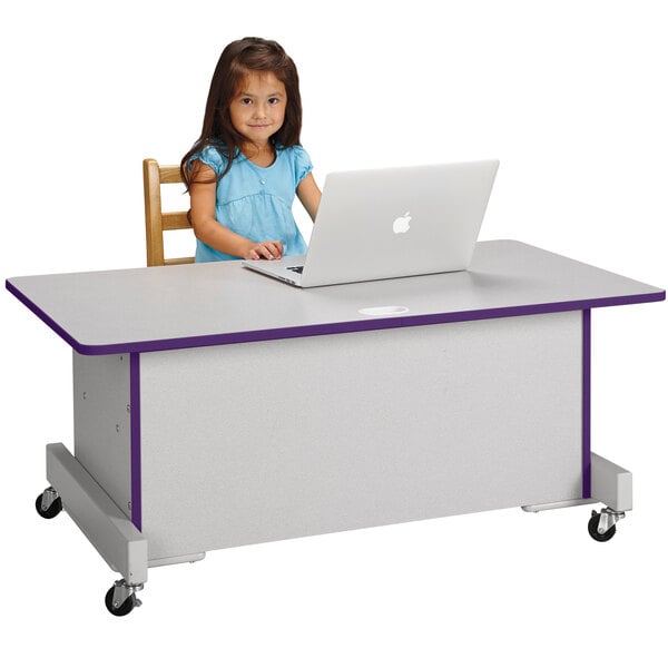 A young girl sitting at a Rainbow Accents adjustable height computer desk using a laptop.
