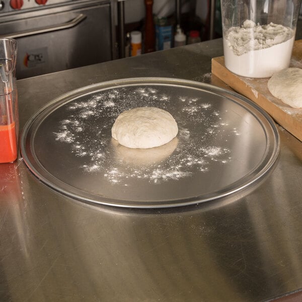 A dough ball on an American Metalcraft aluminum pizza pan on a counter.