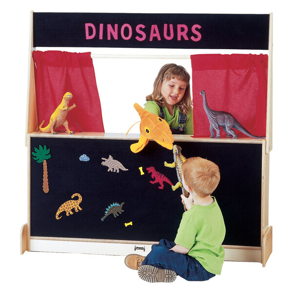 A boy and girl playing with dinosaurs on a stage with a black flannel background.