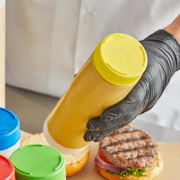A person in black gloves using a Tablecraft yellow end cap to dispense mustard.