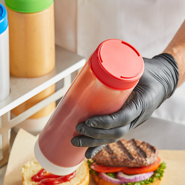 A hand in a black glove holding a Tablecraft squeeze bottle with a red lid.