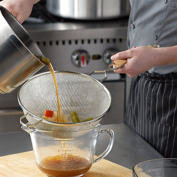 A person pouring liquid into a Tablecraft fine tin double mesh strainer.