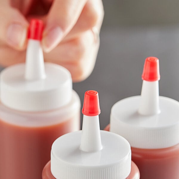 A person using a Tablecraft red cone tip to pour sauce into a white plastic squeeze bottle with a white cap.