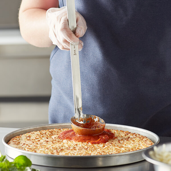 A person using a Vollrath stainless steel ladle to pour sauce over food on a pizza.