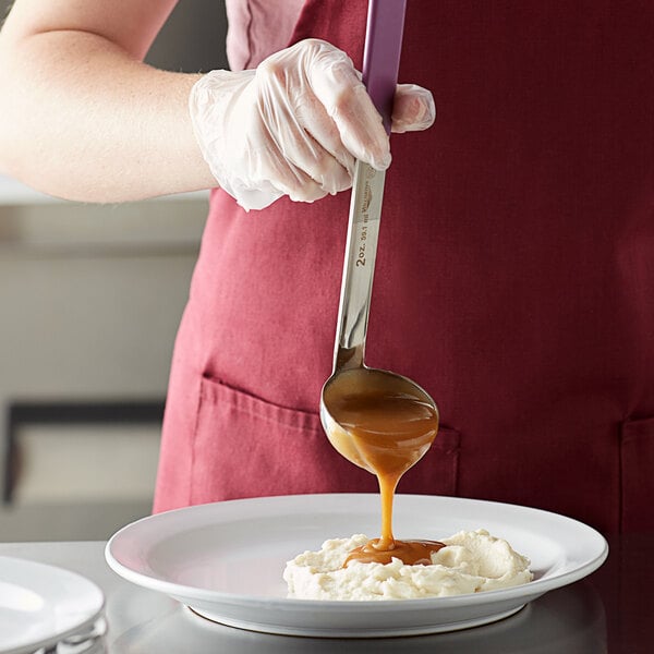 A person using a Vollrath Jacob's Pride ladle with a purple Kool-Touch handle to pour syrup over food.
