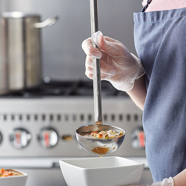 A person using a Vollrath stainless steel ladle to serve soup.